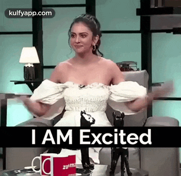 a woman in a white dress is sitting in a chair with her arms outstretched and the words `` i am excited '' .