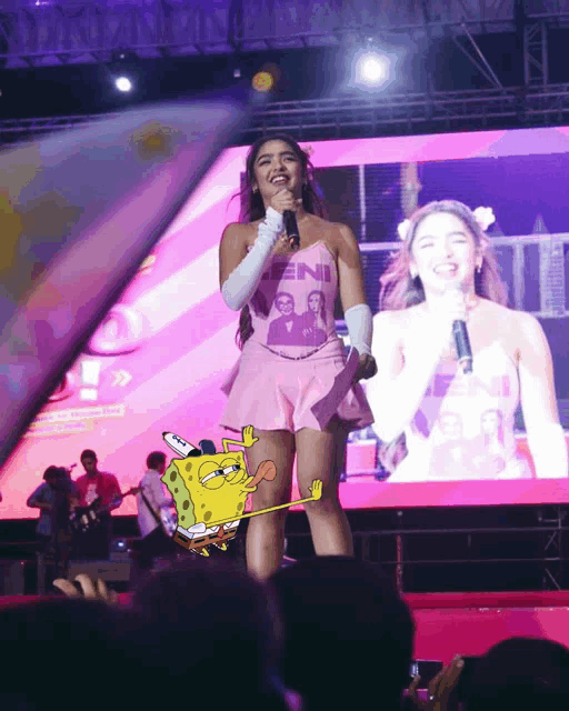 a woman wearing a pink top that says feni singing into a microphone