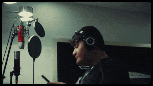 a man wearing headphones looks at a cell phone in front of a microphone