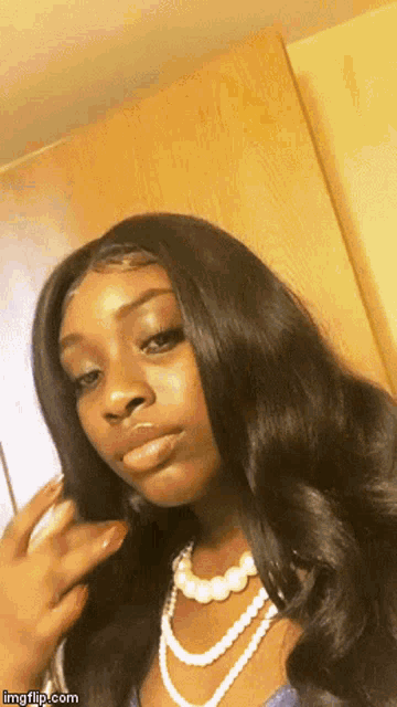 a woman wearing a pearl necklace and a wig looks at the camera .