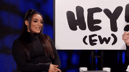 a woman sitting in front of a sign that says hey