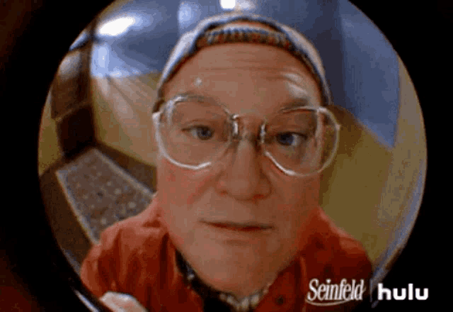 a man with glasses and a hat is looking through a peephole with seinfeld hulu written on it