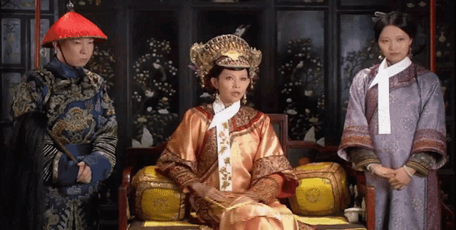 a woman wearing a crown sits in a chair while a man stands behind her