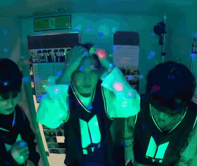 a group of people are standing in a dark room with a poster on the wall that says ' bts '