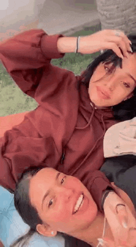 two women are laying on top of each other on a blanket and smiling .