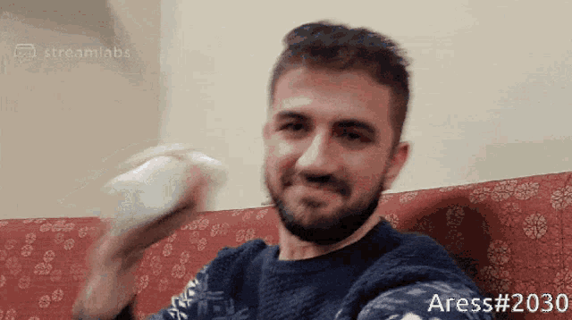 a man with a beard is sitting on a couch holding a white object and the number 2030 is on the bottom