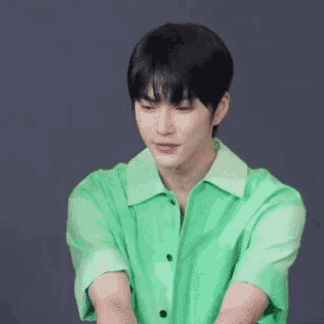 a young man in a green shirt is sitting at a table with his hands in the air .