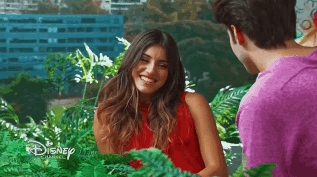 a woman in a red dress is smiling next to a man in a purple shirt with the disney channel written on the bottom