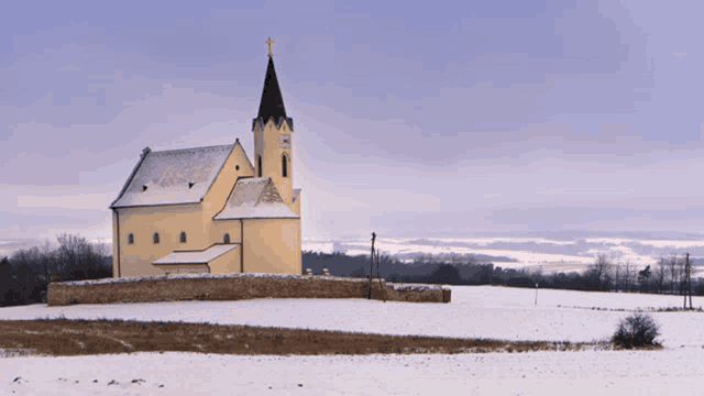 a small yellow church with a black steeple and a cross on top