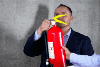 a man in a suit is holding a red fire extinguisher with a yellow tip
