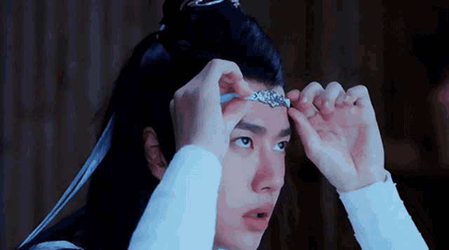 a man wearing a white shirt is adjusting a necklace on his head