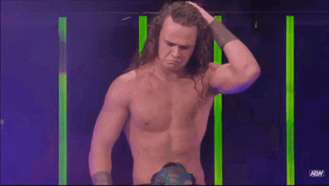 a shirtless wrestler with long hair is standing in front of a purple and green background .