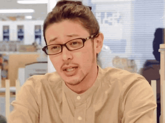 a man wearing glasses and a tan shirt is looking at the camera