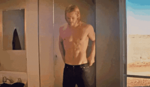 a shirtless man is standing in a bathroom in front of a mirror .