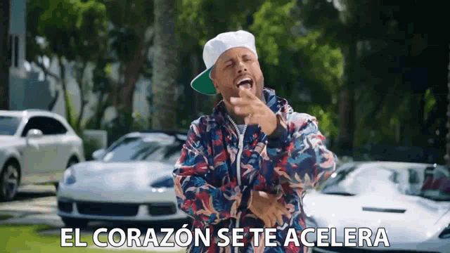 a man wearing a hat and a colorful jacket is standing in front of a bunch of white cars and laughing .