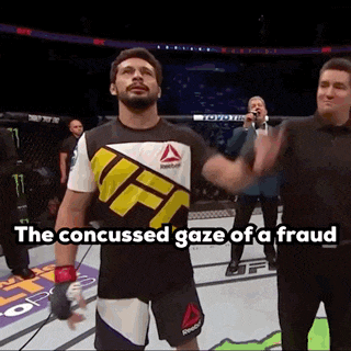 a man in a ufc shirt is standing in a ring with a referee .