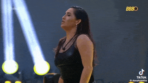 a woman in a black tank top is standing on a stage in front of a spotlight .