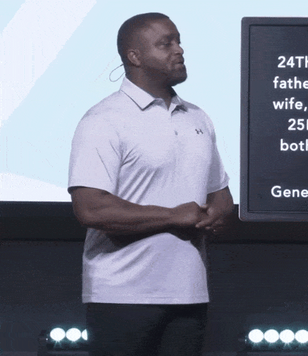 a man in a white under armour shirt stands in front of a large screen