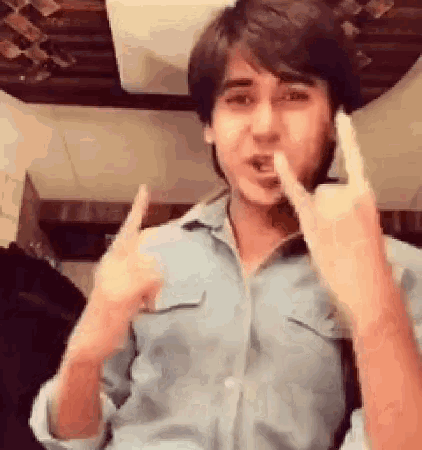 a young man is making a devil horns sign with his fingers .
