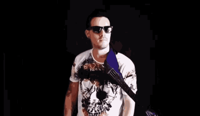 a man wearing sunglasses and a guitar strap is standing in front of a black background .