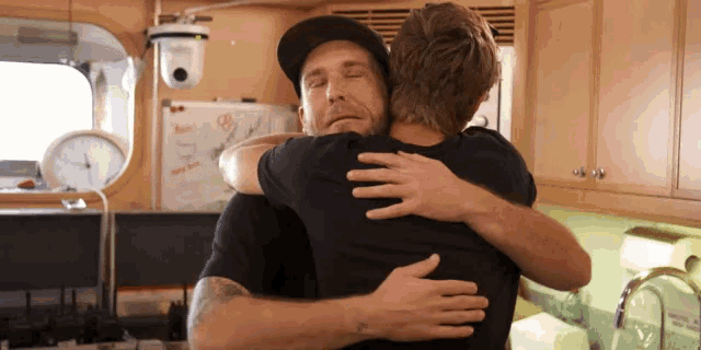 two men hugging each other in a kitchen with a clock on the wall behind them that says 3:00