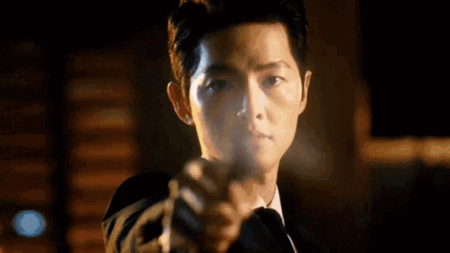 a man in a suit and tie is pointing a gun at the camera at night .
