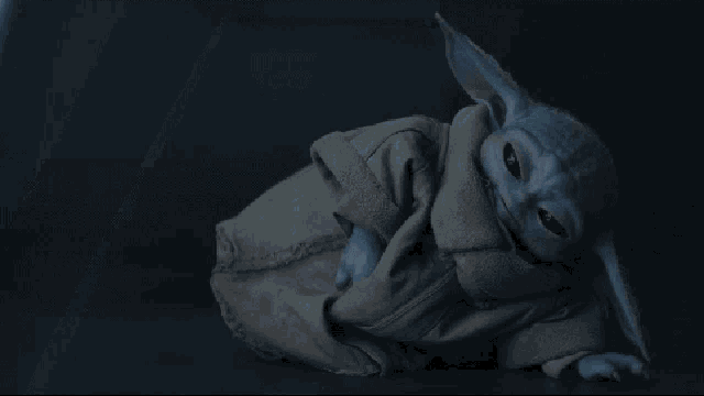 a baby yoda is laying down in a dark room