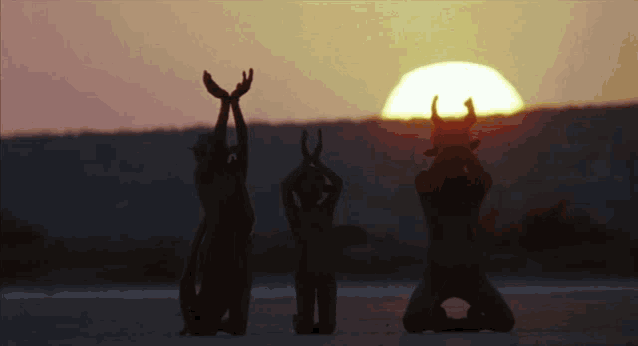 three naked people with horns on their heads are kneeling in front of the sun