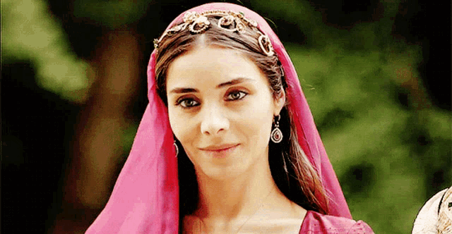 a woman wearing a pink head scarf and earrings is smiling
