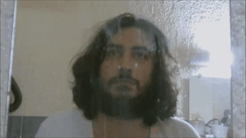 a man with long hair and a beard looks at himself in the mirror
