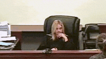 a woman sits in a chair in a courtroom with her hand on her chin