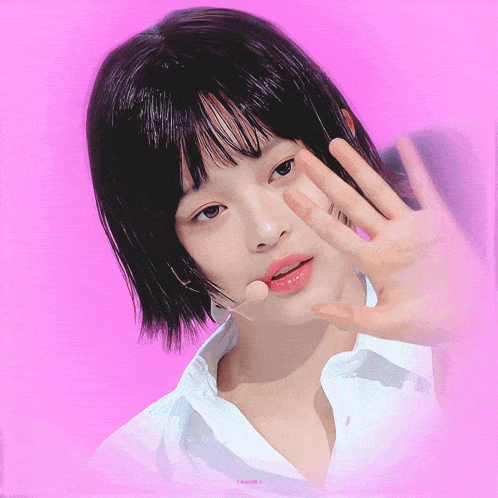 a girl with short black hair is wearing a white shirt and making a waving gesture