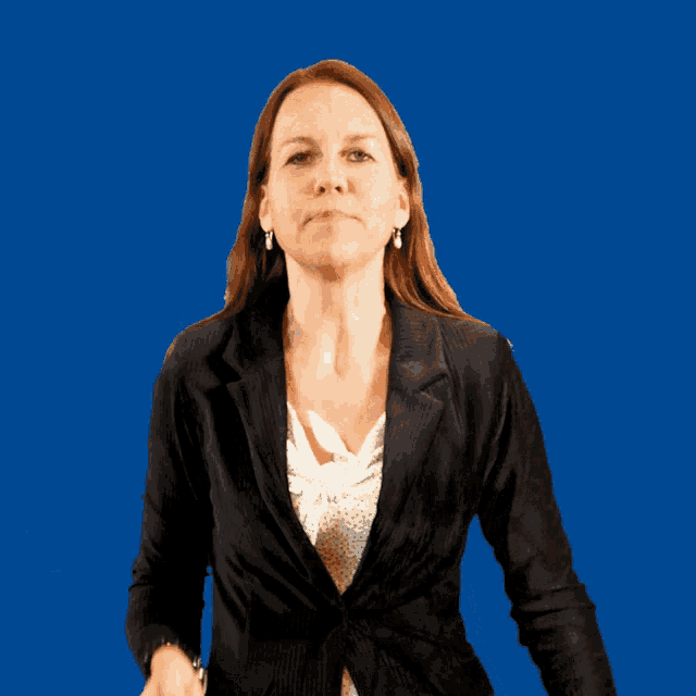 a woman in a black jacket stands in front of a blue backdrop