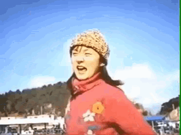 a woman wearing a hat and a red jacket with a flower on the sleeve