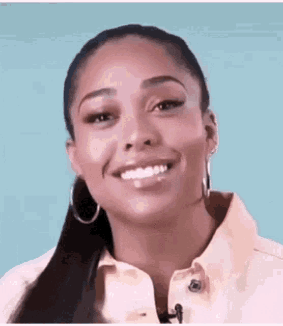 a woman wearing hoop earrings and a yellow shirt is smiling and looking at the camera .