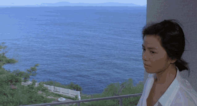 a woman in a white shirt looks out over the ocean