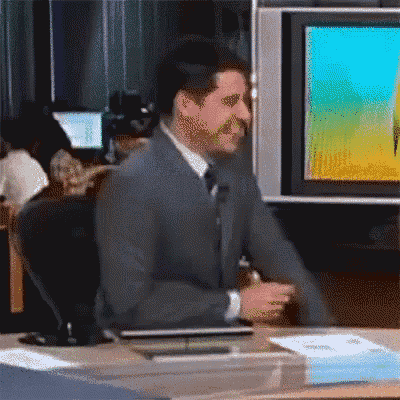 a man in a suit and tie is sitting at a desk in front of a tv