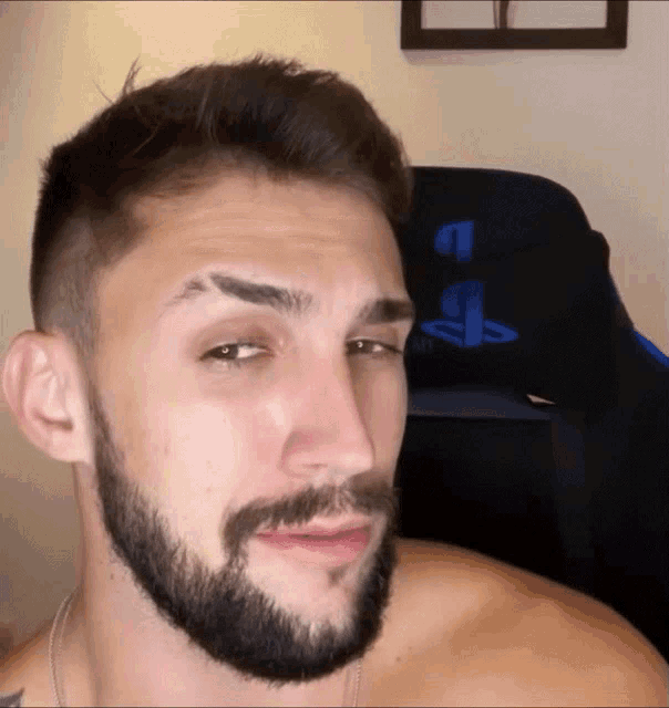 a shirtless man with a beard looks at the camera in front of a playstation logo