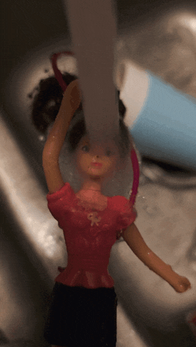 a barbie doll is being washed in a sink with water coming out of the faucet