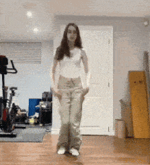 a woman in a white top and khaki pants is dancing in a room