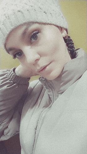 a woman wearing a knitted hat and a jacket looks at the camera