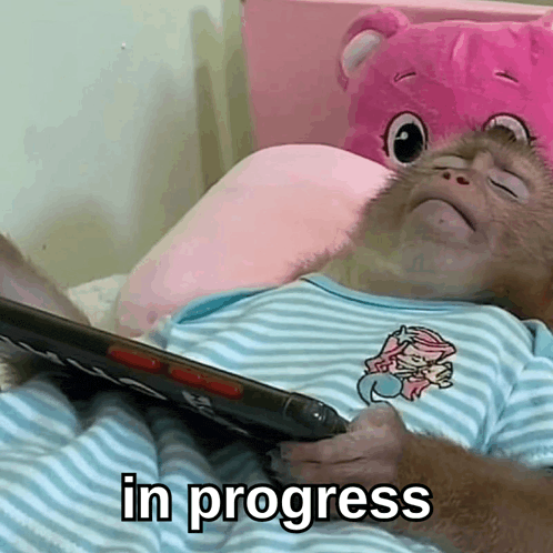a baby monkey is laying on a bed holding a tablet and the words " in progress " are above it