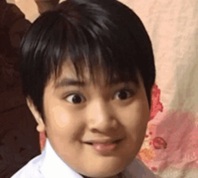 a young boy with short black hair and a white shirt is smiling .