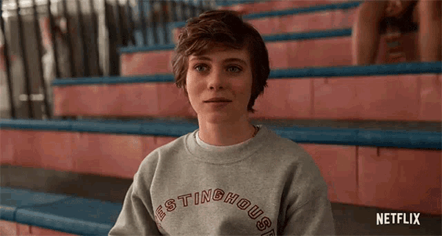 a young girl is sitting on a set of bleachers wearing a sweatshirt that says wrestlinghouse .