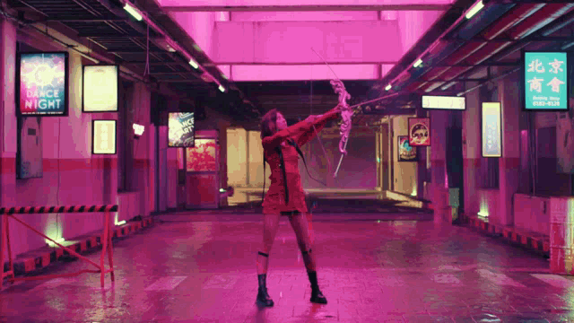 a woman in a red dress holds a bow and arrow in front of a sign that says dance night