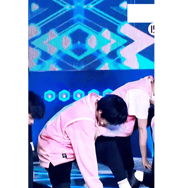 a man in a pink sweatshirt is kneeling down on a stage