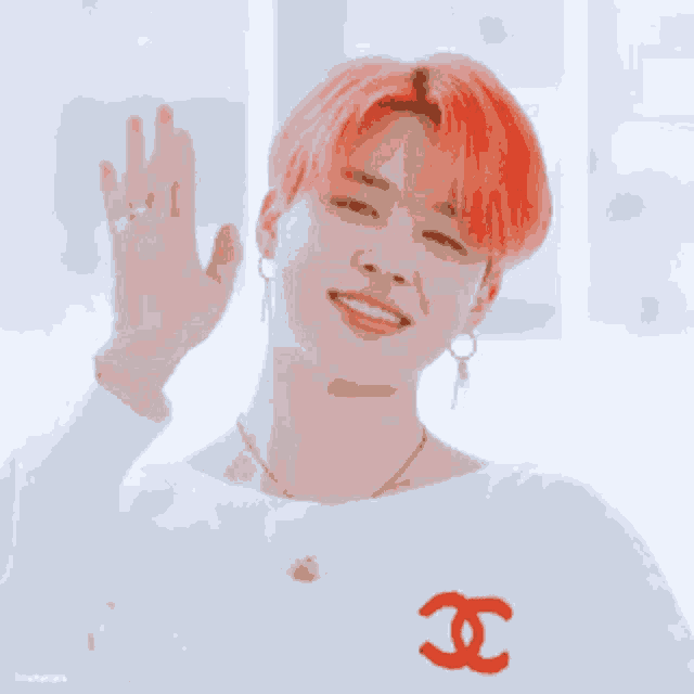 a young man with red hair is wearing a white sweater with a red chanel logo on the chest .