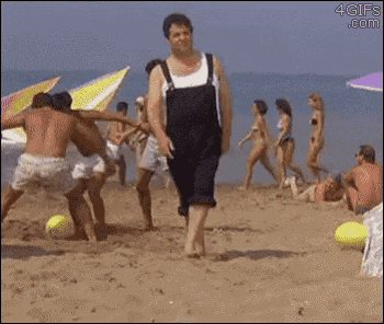 a man in black overalls is kicking a yellow ball on a beach .