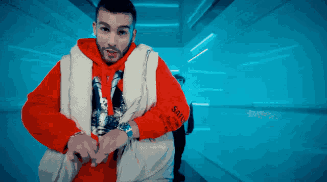 a man wearing a red hoodie and a white vest with the word saints on it
