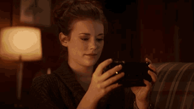 a woman sitting on a couch playing a video game on her phone